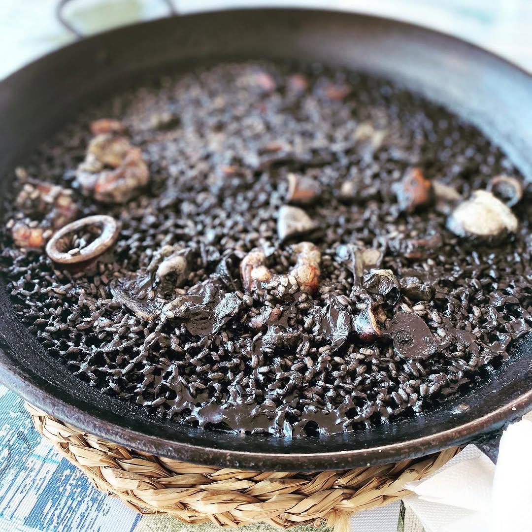 Arroz negro de sepia y su tinta de El Galeón, servido en paella sobre mantel de cuadros azul